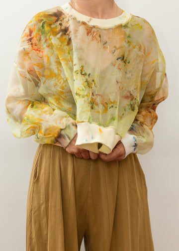 Model wearing a see-through silk top with notes of yellow, green and orange in a tie-dye type style.