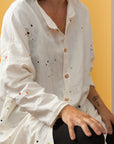 Close-up of model wearing a cream colored long button-down shirt with 3/4 sleeves and paint splatter.