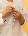 Close-up of model wearing a cream colored long button-down shirt with 3/4 sleeves and paint splatter.