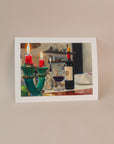 Photo of an art print for an italian series of a bottle of wine with a candle holder in the foreground. Print is on a light pink background