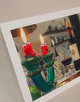 Photo of an art print for an italian series of a bottle of wine with a candle holder in the foreground. Print is in front of a light pink background