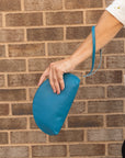 Woman holding a shell shaped handbag in a vivid blue color by the top with a wrist pull