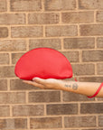 Woman holidng a shell-shaped handbag in cherry in her palm with a leather pull wrapped around her wrist