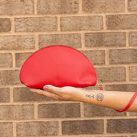 Woman holidng a shell-shaped handbag in cherry in her palm with a leather pull wrapped around her wrist