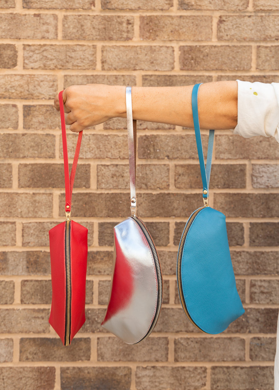 three colored shell-shaped handbags all hanging from a womans arm by the leather pulls. Colors are cherry, silver and azure