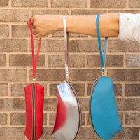 three colored shell-shaped handbags all hanging from a womans arm by the leather pulls. Colors are cherry, silver and azure