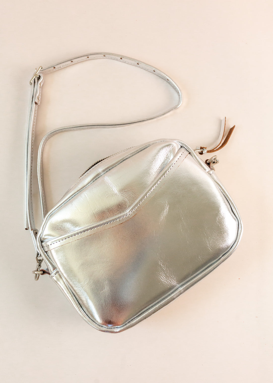 Flatlay of cubist handbag in silver, with a v-shaped front pocket and a long thin shoulder strap
