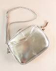 Flatlay of cubist handbag in silver, with a v-shaped front pocket and a long thin shoulder strap