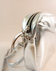 Close-up of cubist handbag in silver, with a v-shaped front pocket and a long thin shoulder strap
