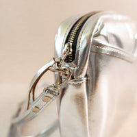 Close-up of cubist handbag in silver, with a v-shaped front pocket and a long thin shoulder strap