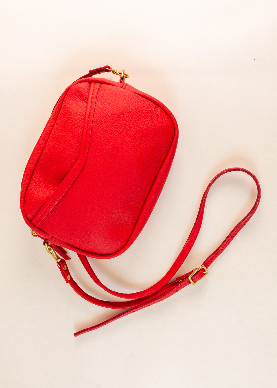 Flatlay of cubist handbag in cherry, with a v-shaped front pocket and a long thin shoulder strap