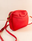 Close up of cubist handbag in cherry, with a v-shaped front pocket and a long thin shoulder strap