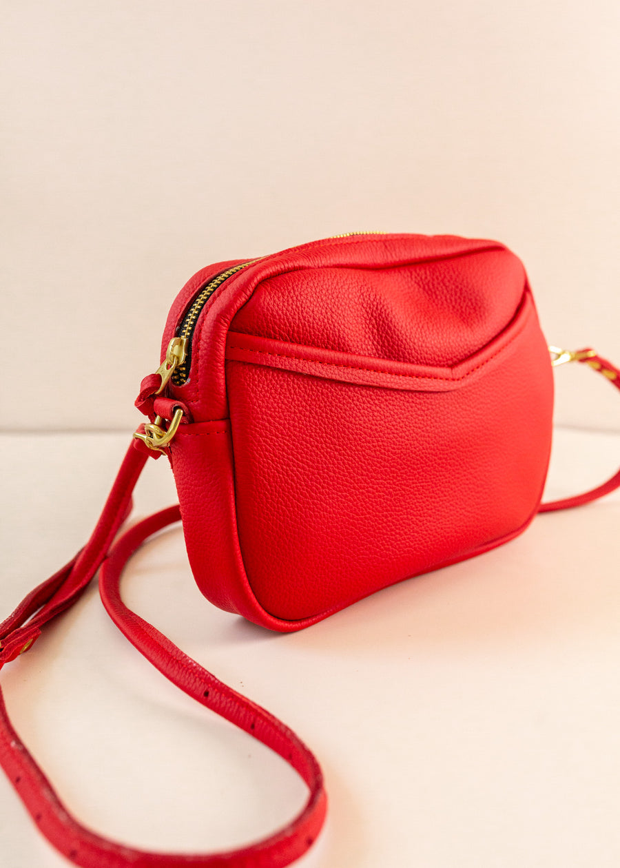 Close up of cubist handbag in cherry, with a v-shaped front pocket and a long thin shoulder strap