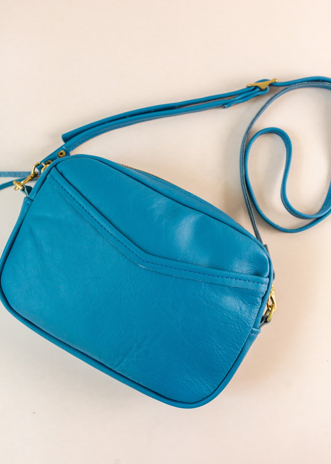 Flatlay of cubist handbag in azure, or blue, with a v-shaped front pocket and a long thin shoulder strap