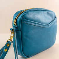 Close-up of cubist handbag in azure, with a v-shaped front pocket and a long thin shoulder strap