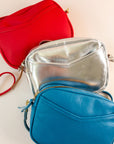 Layer of cubist handbags, with a v-shaped front pocket and a long thin shoulder strap, in cherry, silver and azure