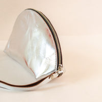 Close-up on the zipper of a silver Shell Bag standing flat on a light pink background with a short wrist handle
