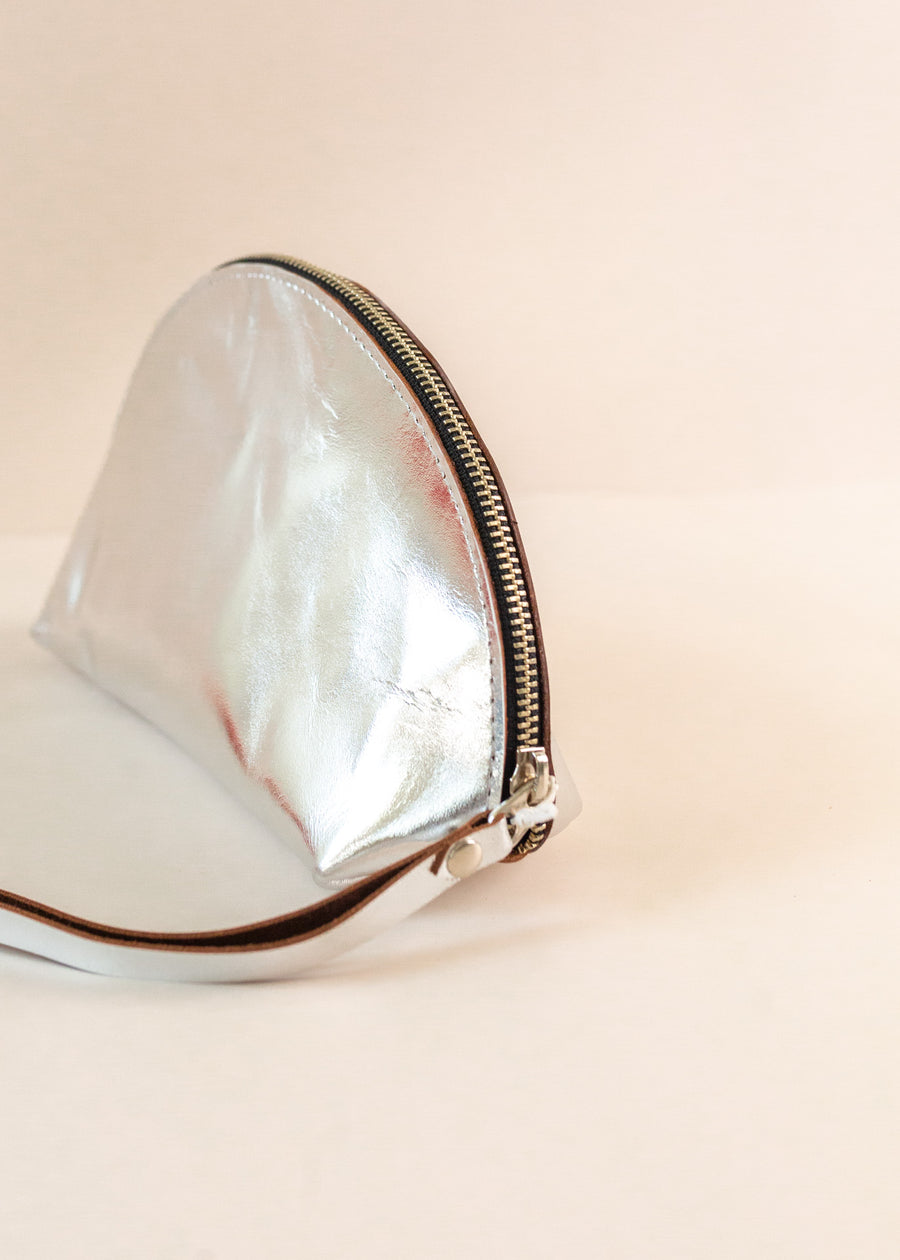 Close-up on the zipper of a silver Shell Bag standing flat on a light pink background with a short wrist handle