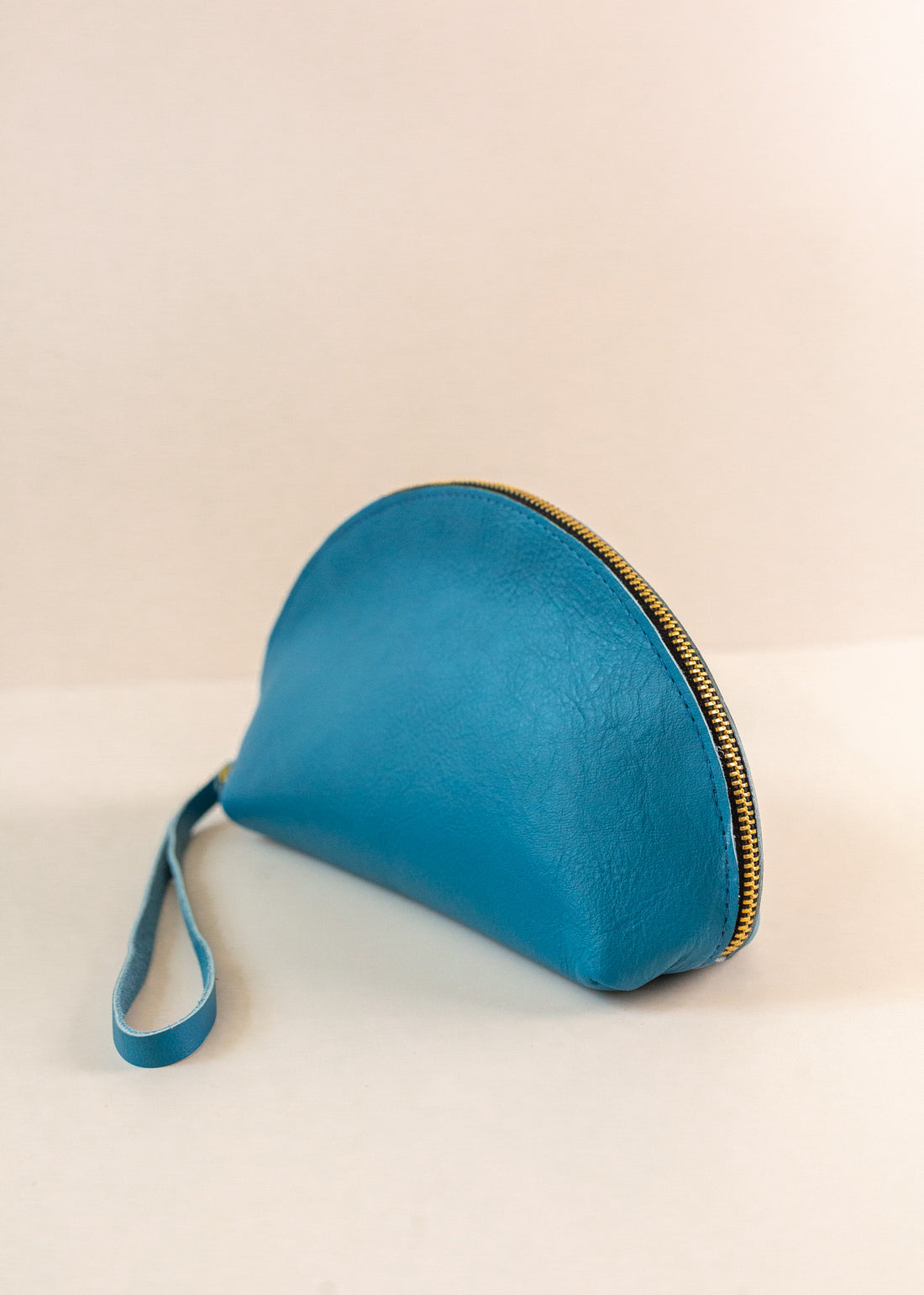 Azure, or blue, colored shell bag standing up on a light pink background with a short wrist handle