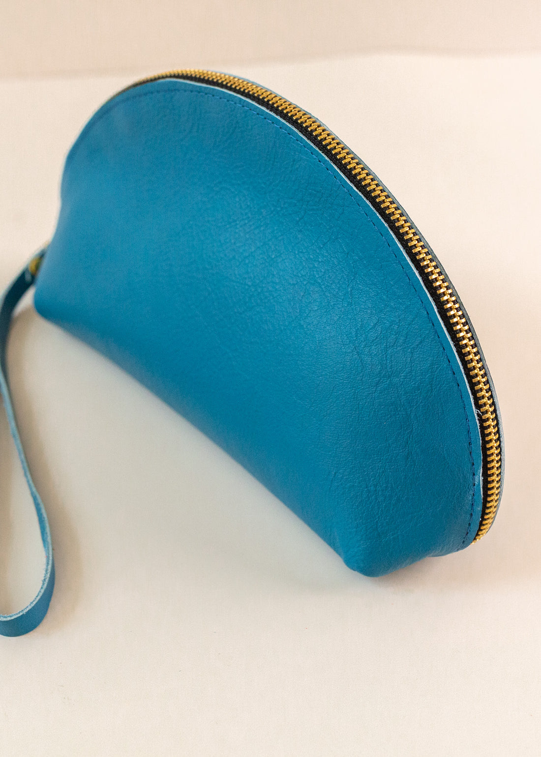 Close-up of Azure, or blue, colored shell bag standing up on a light pink background with a short wrist handle