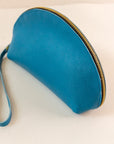 Close-up of Azure, or blue, colored shell bag standing up on a light pink background with a short wrist handle