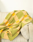 Lime green, cream and mustard colored blanket draped over a couch