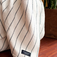 Close-up of a cream colored throw with blue stripes throughout, hanging out of a basket