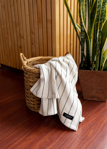 Cream colored throw with blue stripes throughout, falling out of a basket onto the floor