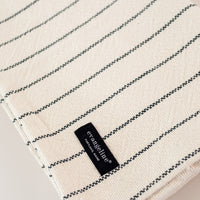 Folded up cream colored throw with blue stripes throughout, laying on a white background