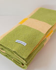 Folded up green, tan and yellow blanket on a white background