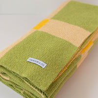 Folded up green, tan and yellow blanket on a white background