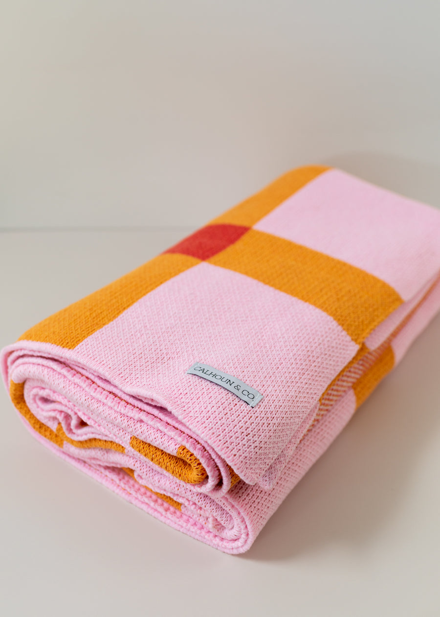 Folded up pink, orange and red blanket on a white background 
