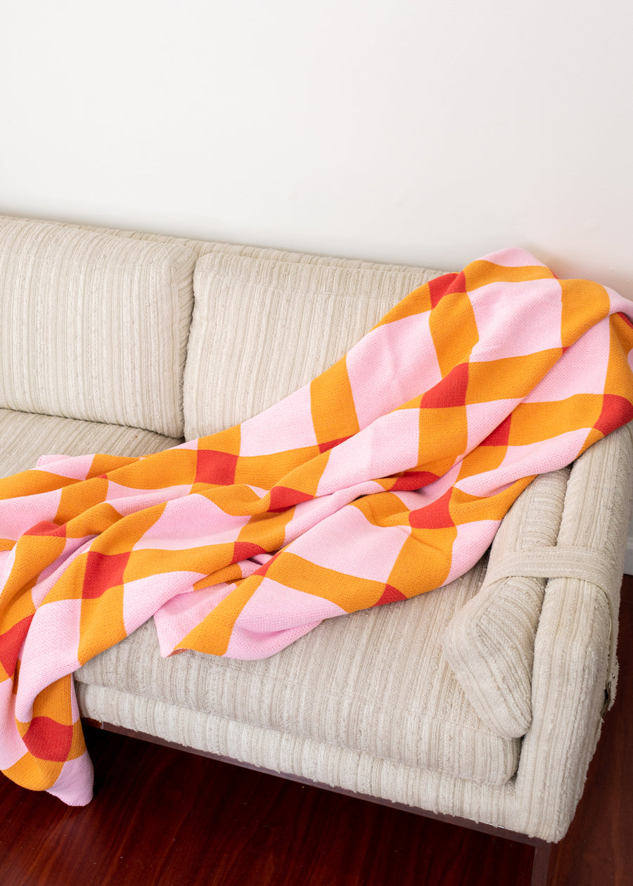 Laid out pink, red and orange patterned blanket on a white couch