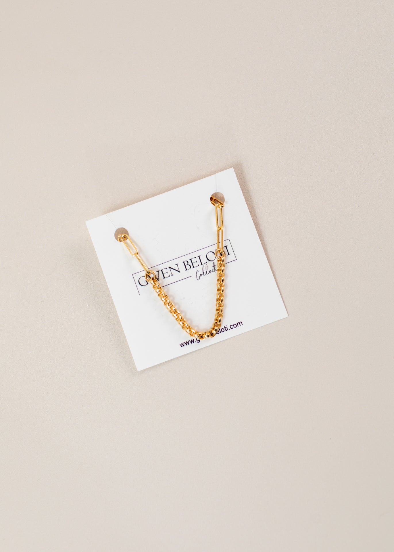 Flatlay of a jewelery card on a light pink background and a gold bracelet chain hanging on card.