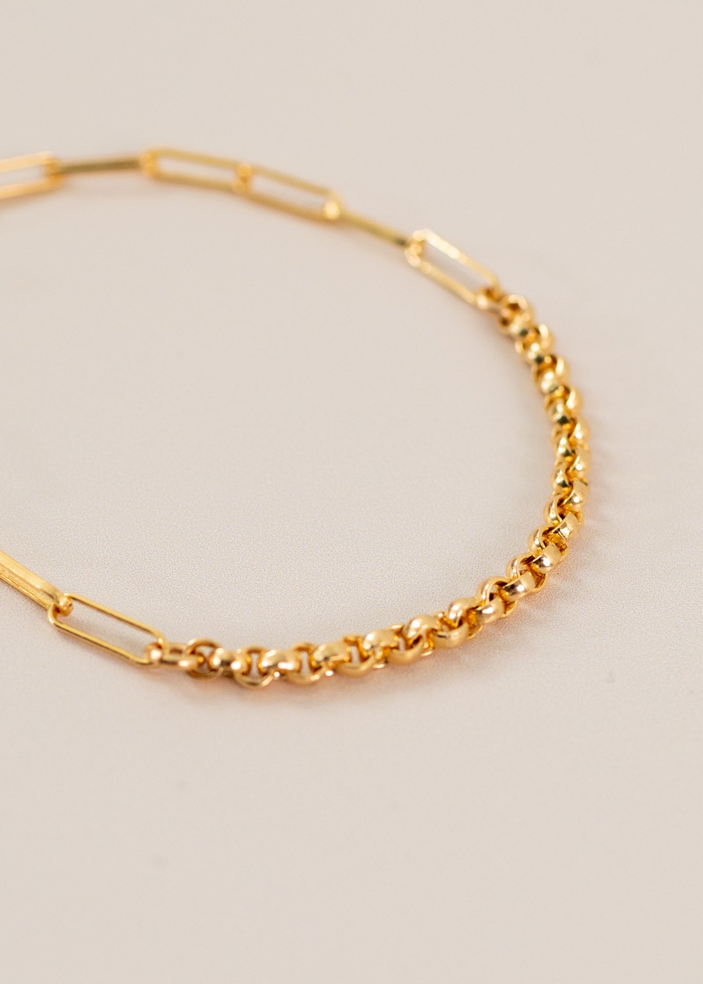 Closeup of a gold bracelet chain on a light pink background