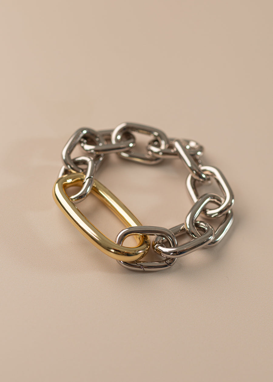 Photo of an oval link bracelet in silver with a large oval link in gold on a peach background