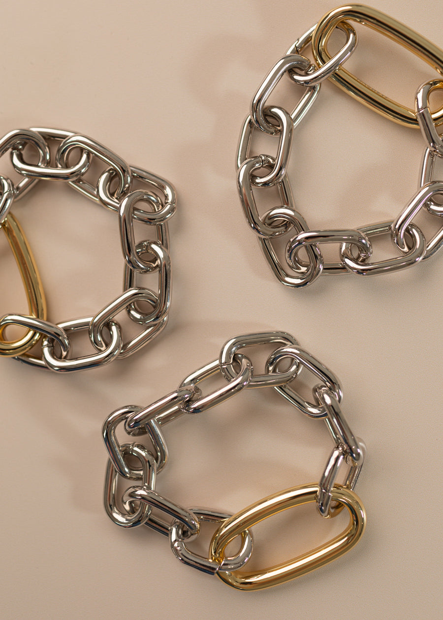 Photo of three oval link bracelets in silver with a large oval link in gold on a peach background