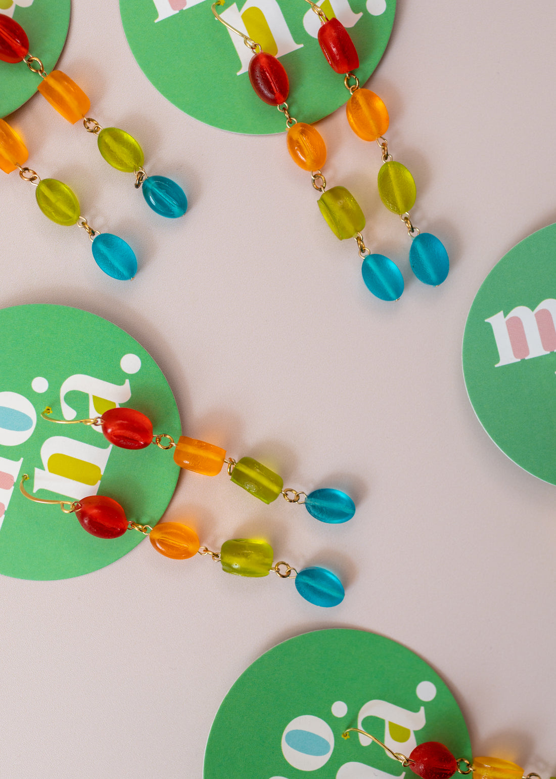 flatlay of multiple, dangly earrings on a green card. Earrings have four beads colored red, orange, green and blue