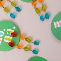 flatlay of multiple, dangly earrings on a green card. Earrings have four beads colored red, orange, green and blue