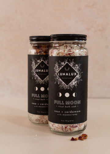 Two tall jars with black labels with one skewed behind the other and a few dried roses and salt in front of them