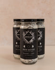 Three tall glass jars in a triangle shape with black labels and bath soaks inside