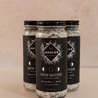 Three tall glass jars in a triangle shape with black labels and bath soaks inside