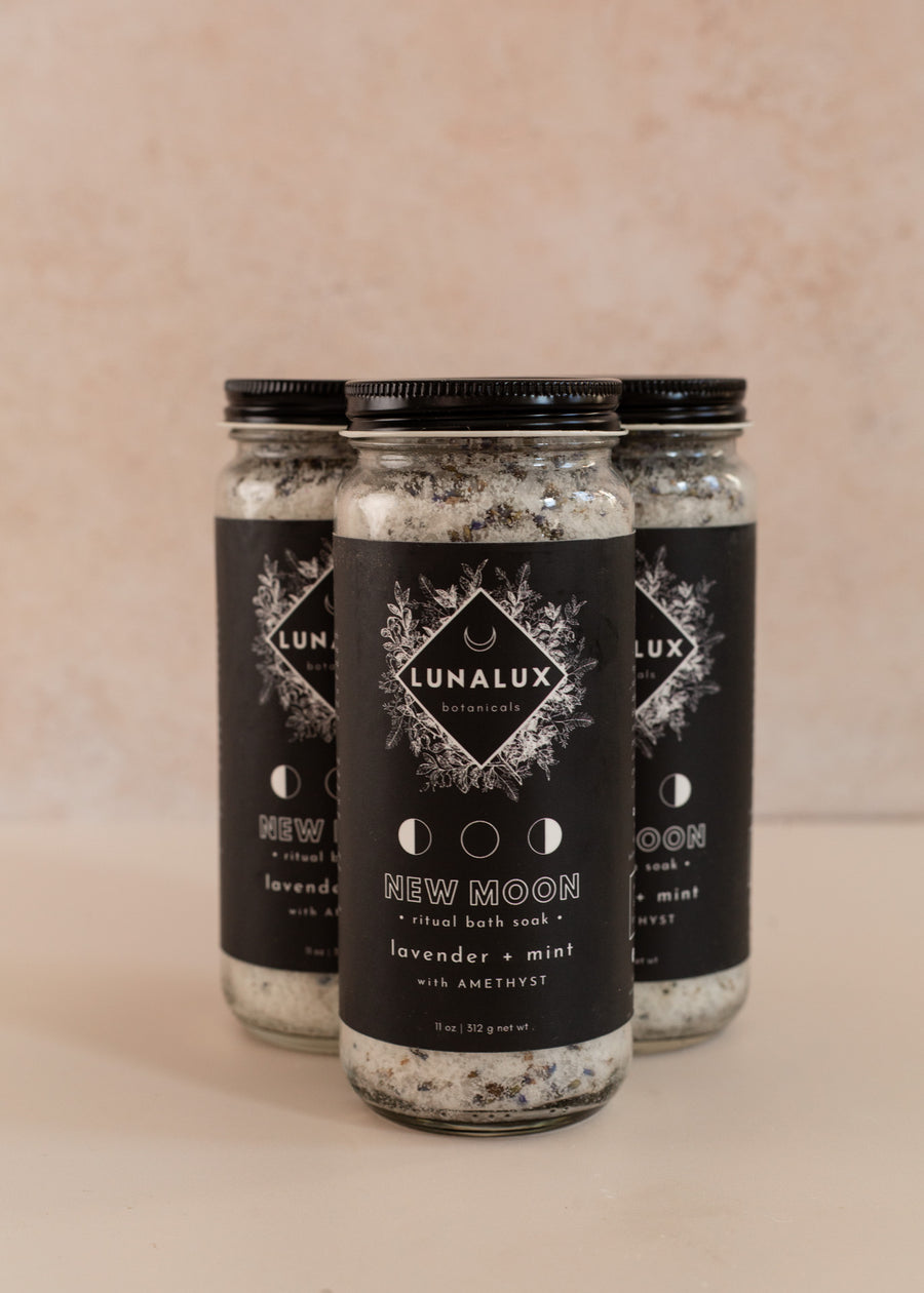 Three tall glass jars in a triangle shape with black labels and bath soaks inside