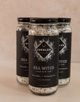Three long glass jars in a triangle shape with black labels and bath soaks inside