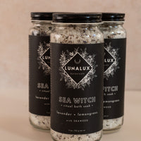 Three long glass jars in a triangle shape with black labels and bath soaks inside