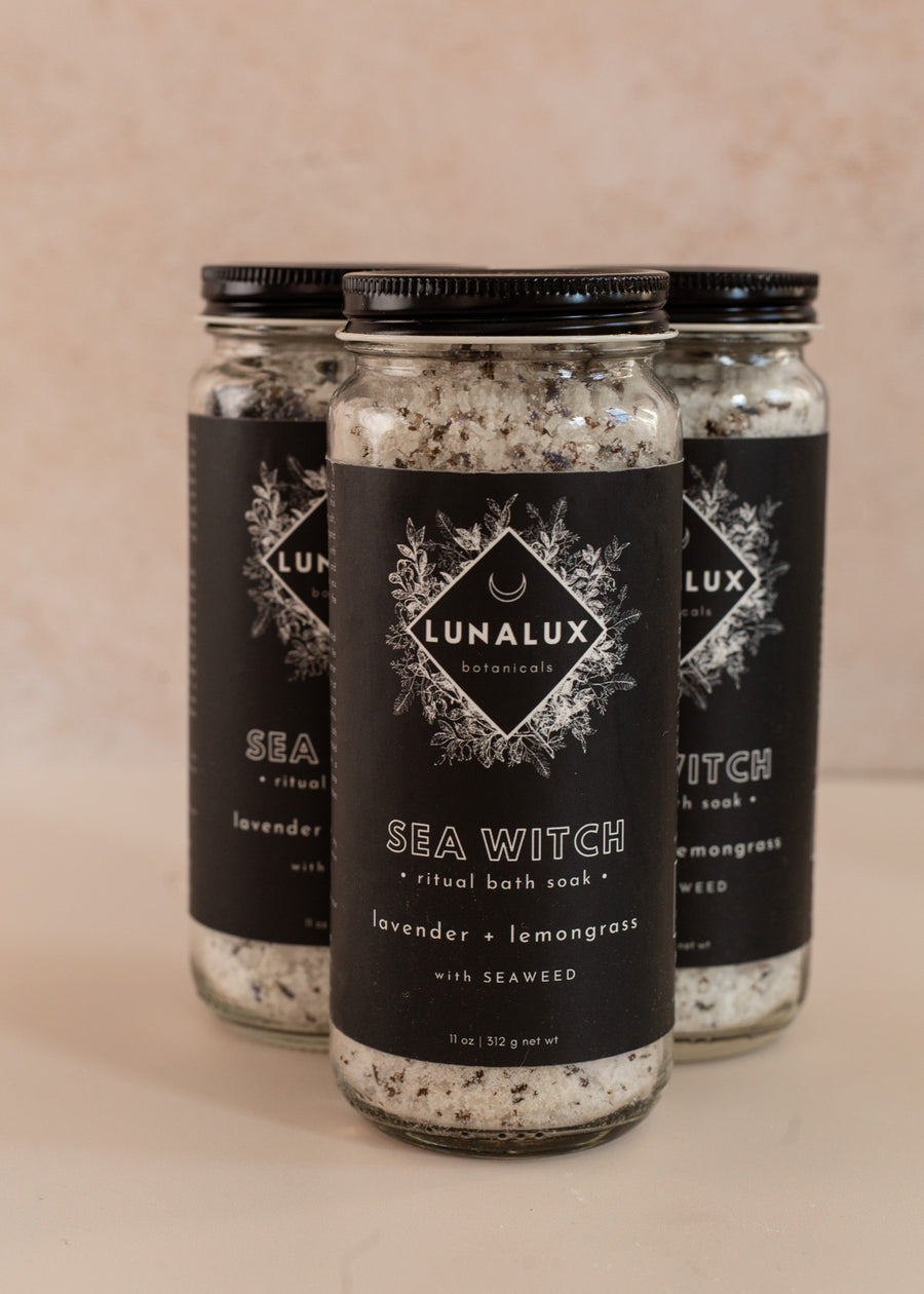 Three long glass jars in a triangle shape with black labels and bath soaks inside
