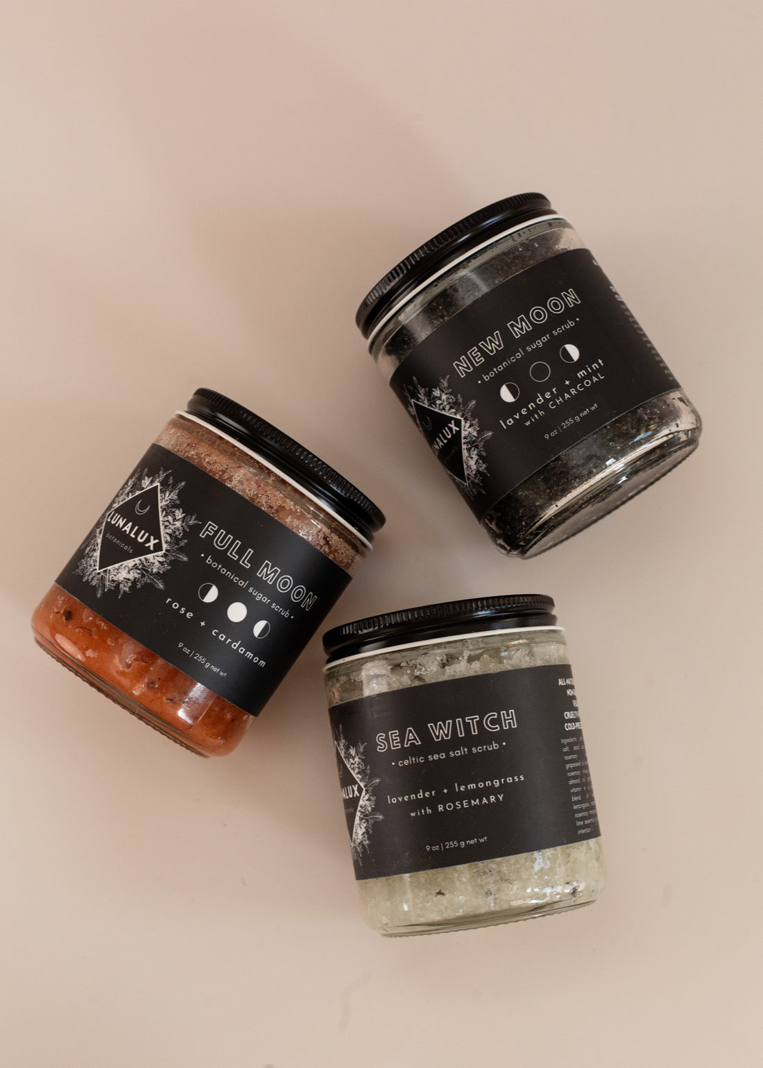 Flat lay of three 9oz glass jars in different scents with black labels, from toop to bottom: new moon, full moon and sea witch