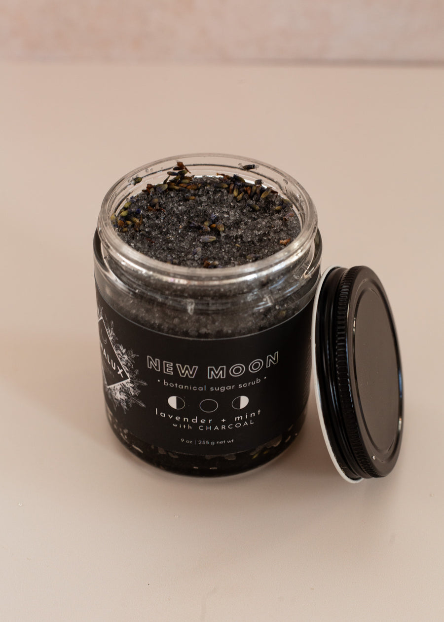 opened 9oz glass jar with black label and the top leaning on the left side, angled up to show the black salt scrub