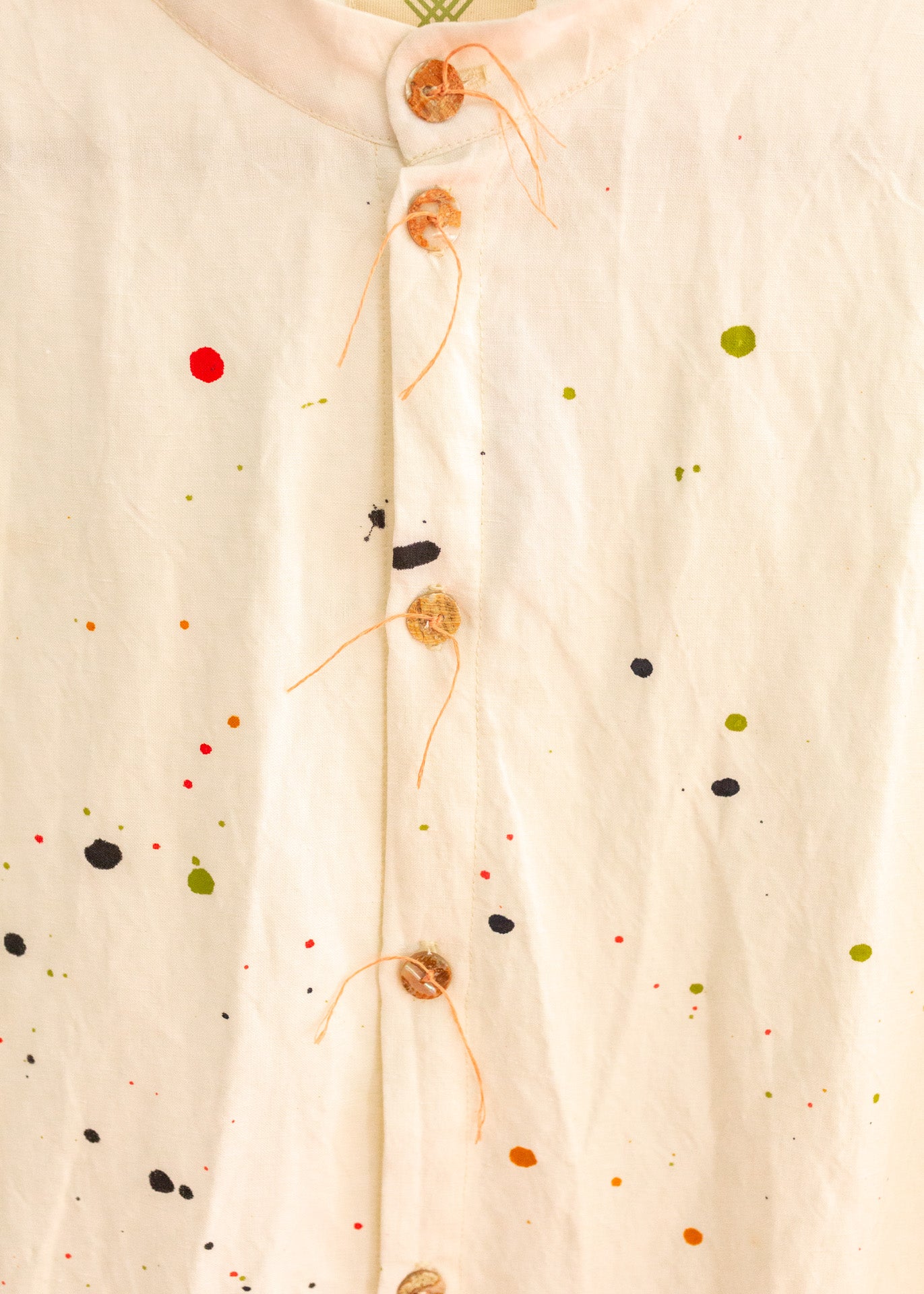 Close-up of the detailed tan buttons on a cream colored long button-down shirt with paint splatter