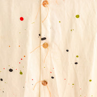 Close-up of the detailed tan buttons on a cream colored long button-down shirt with paint splatter